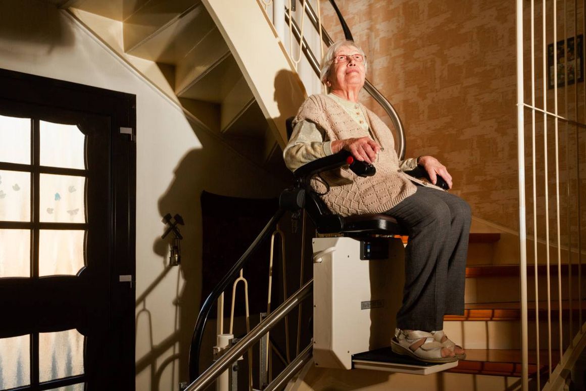 Eine ältere Person fährt in einem Treppenlift eine Treppe hinauf.